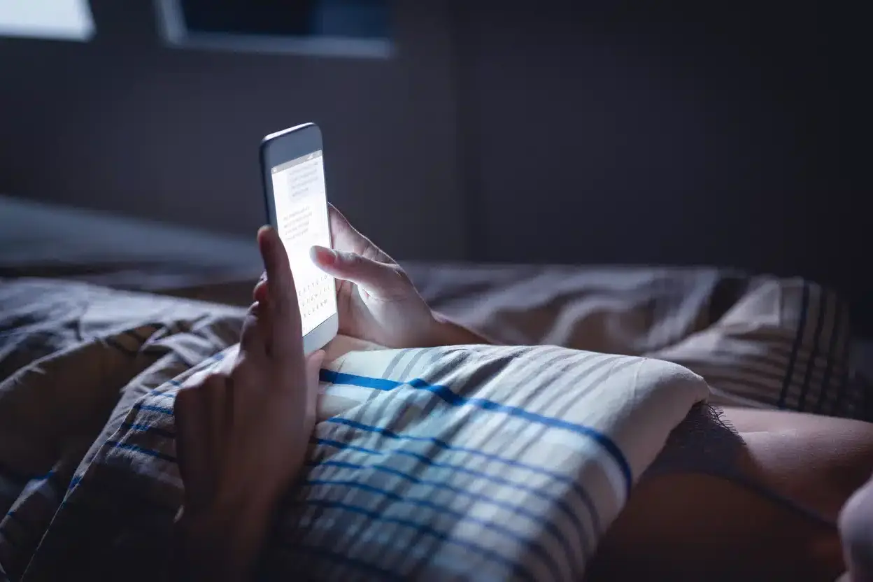 Donna sdraiata a letto che utilizza lo smartphone
